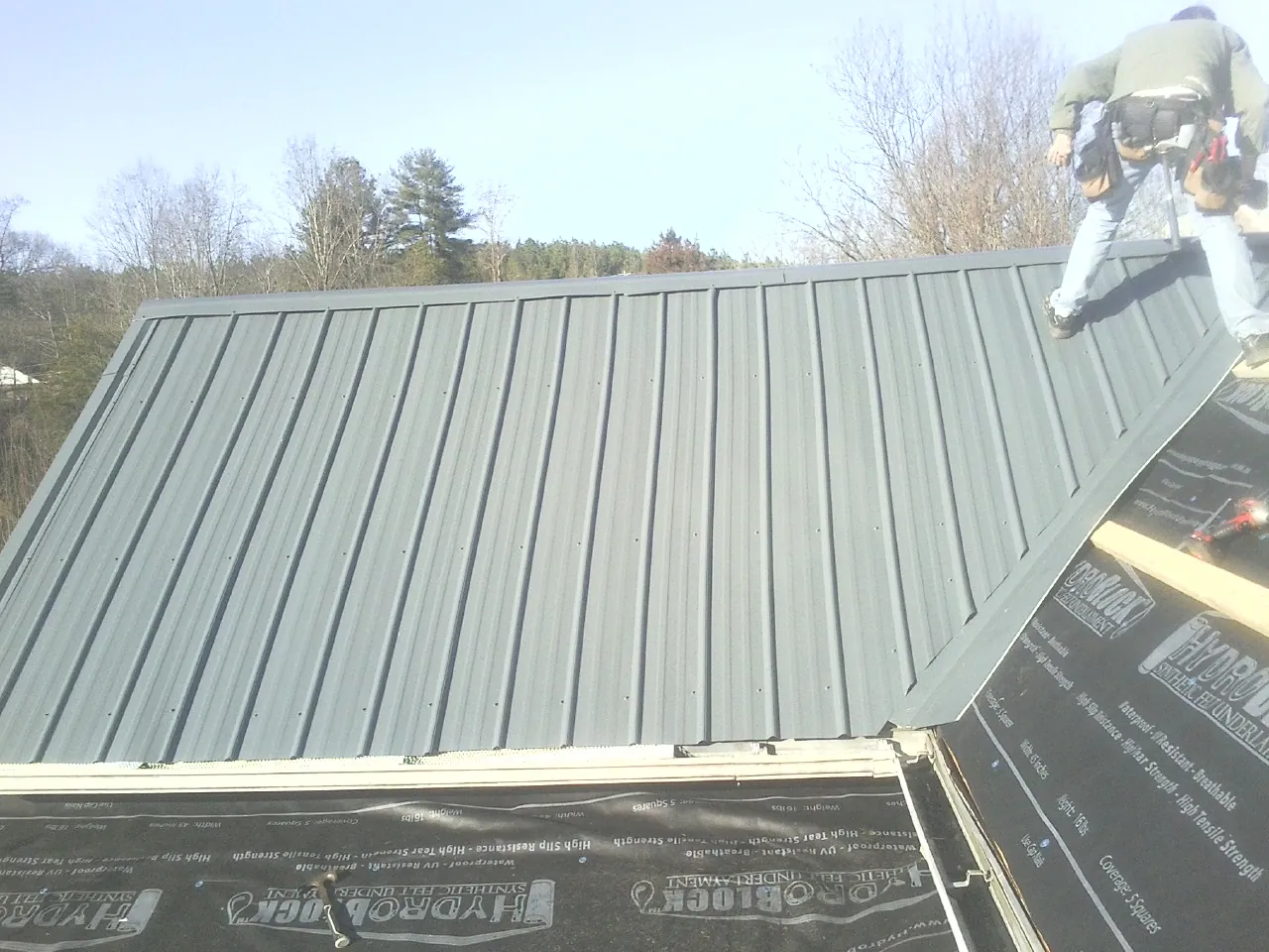 Crew installing dark green standing seam panels over synthetic underlayment in Dameron