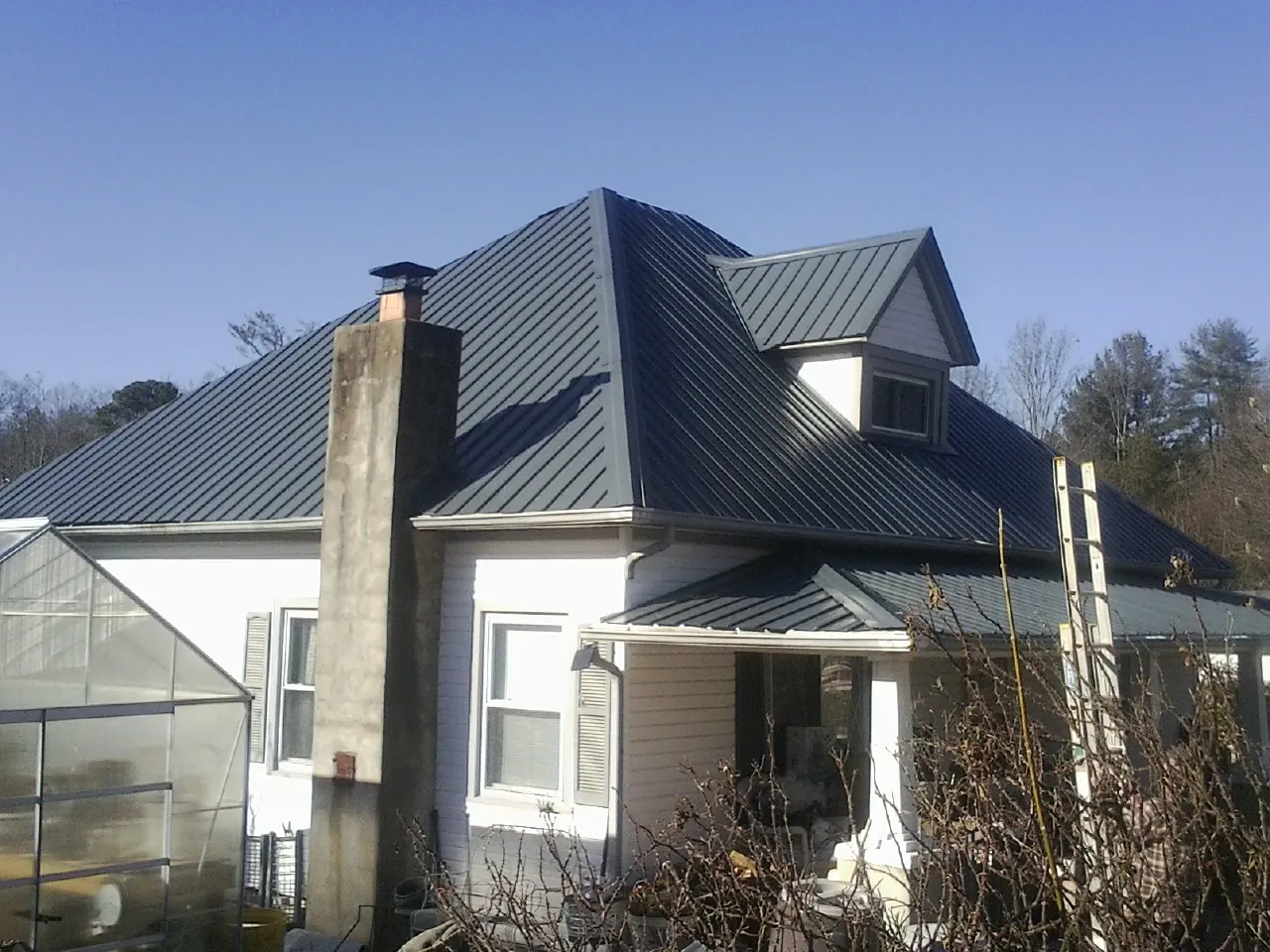 Dark blue standing seam metal roof on a white farmhouse with dormer — Slate & Tile Roof Repair by Roofing Brothers in Dameron