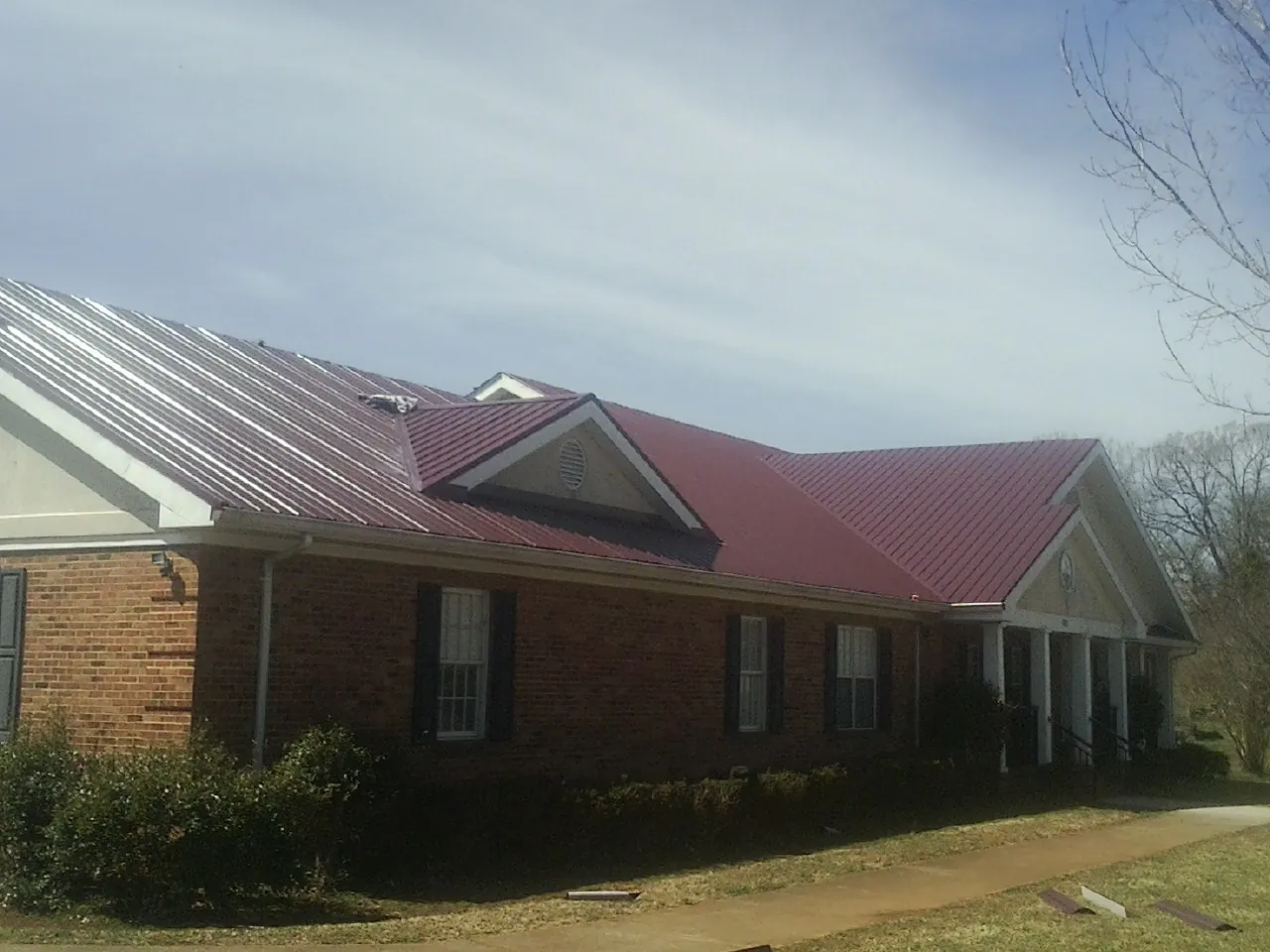 Red metal roof with gabled entries on a long brick building, from a Hail Damage Roof Repair job in Dameron