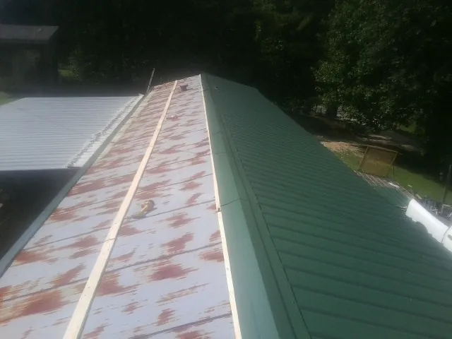 Old rusted panels beside newly installed green metal roofing — Wind Damage Roof Repair by Roofing Brothers in Dameron