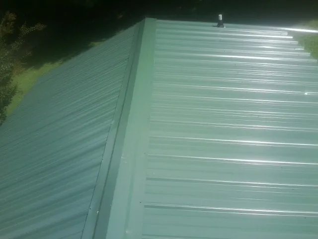 New green metal panels meeting at the ridge of a roof — Flat Roof Repair work by our crew in Dameron