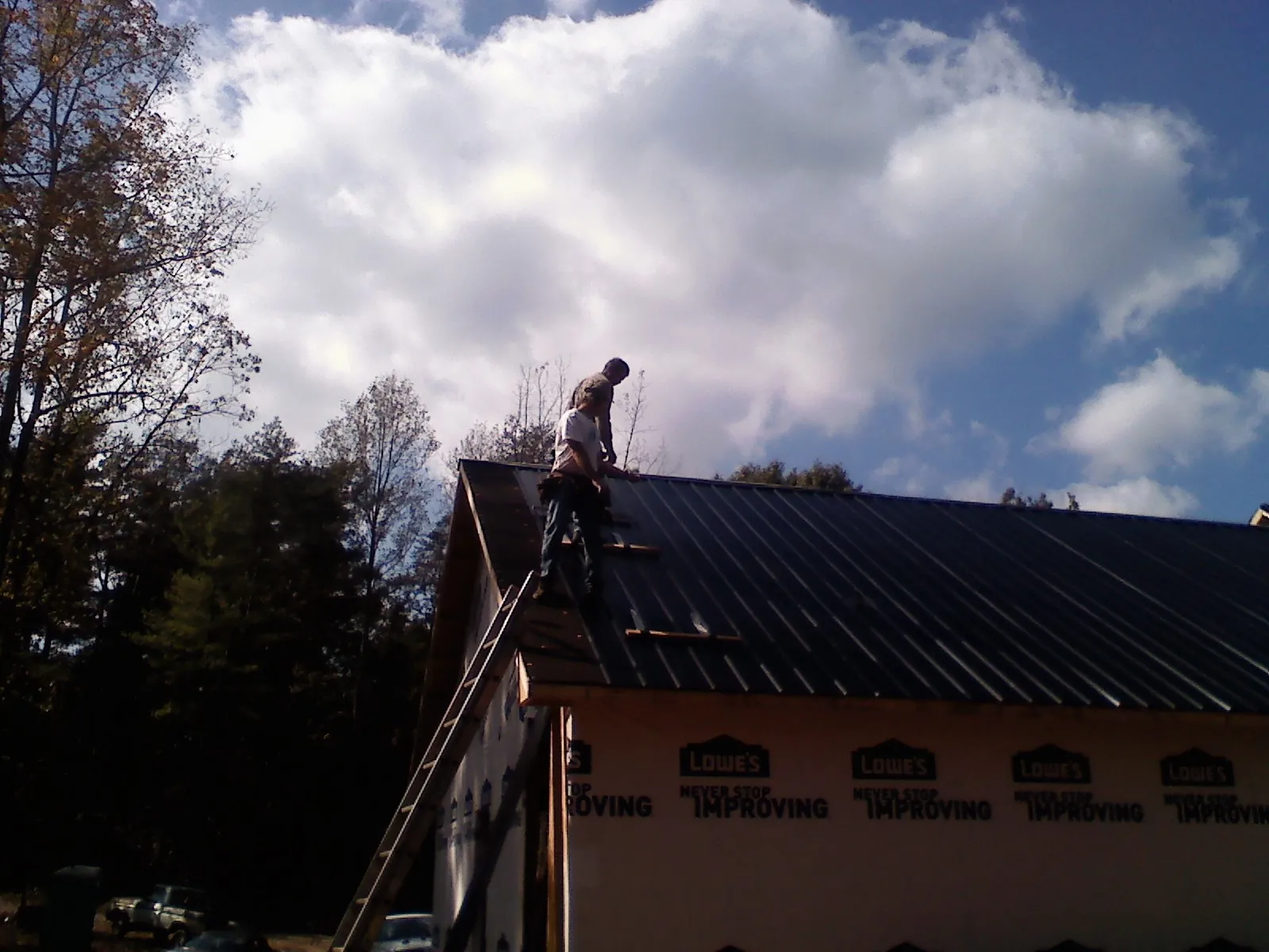 Roofer fastening dark metal panels high against a cloudy sky, from a Roof Inspection job in Dameron